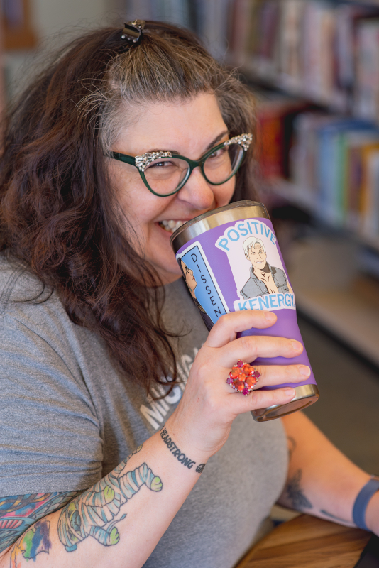 Image of a white woman with long brown hair holding a coffee tumbler to her face.