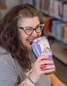 Image of a white woman with long brown hair holding a tumbler near her face. She is smiling.